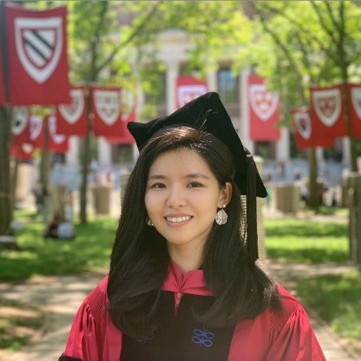 Graduation photo of East Asian woman with straight black hair wearing large white circle earrings and a doctoral cap and gown