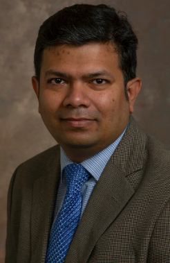 headshot of South Asian man with short black hair wearing a blazer and blue collared shirt and tie